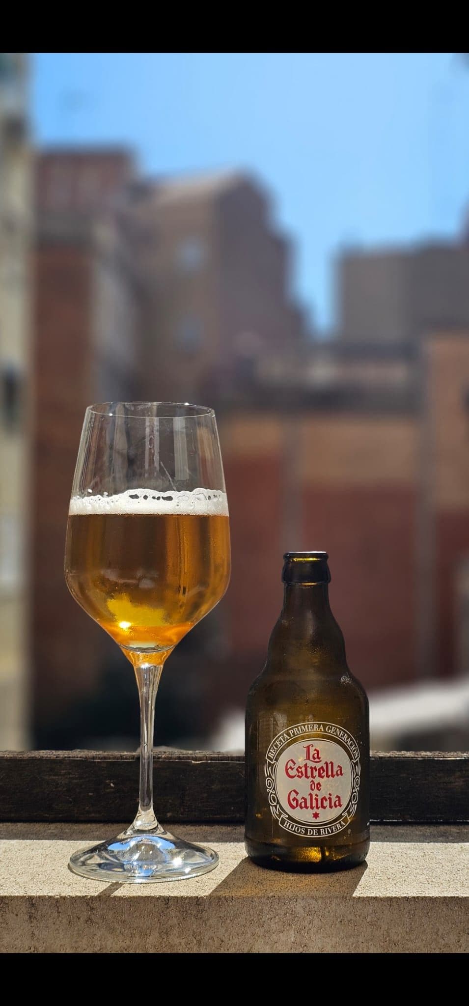Copa de cerveza y botella sobre la barra de un bar, con la calle al fondo